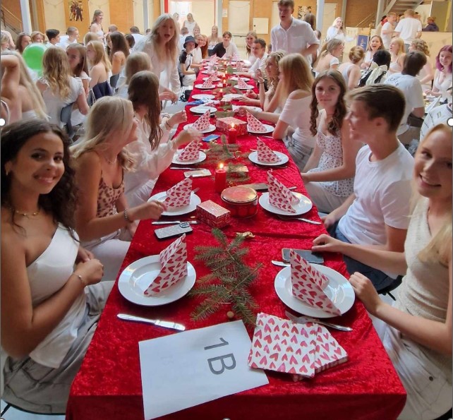 Unge mennesker sidder omkring et pynte bord med rød dug, gran og julepynt